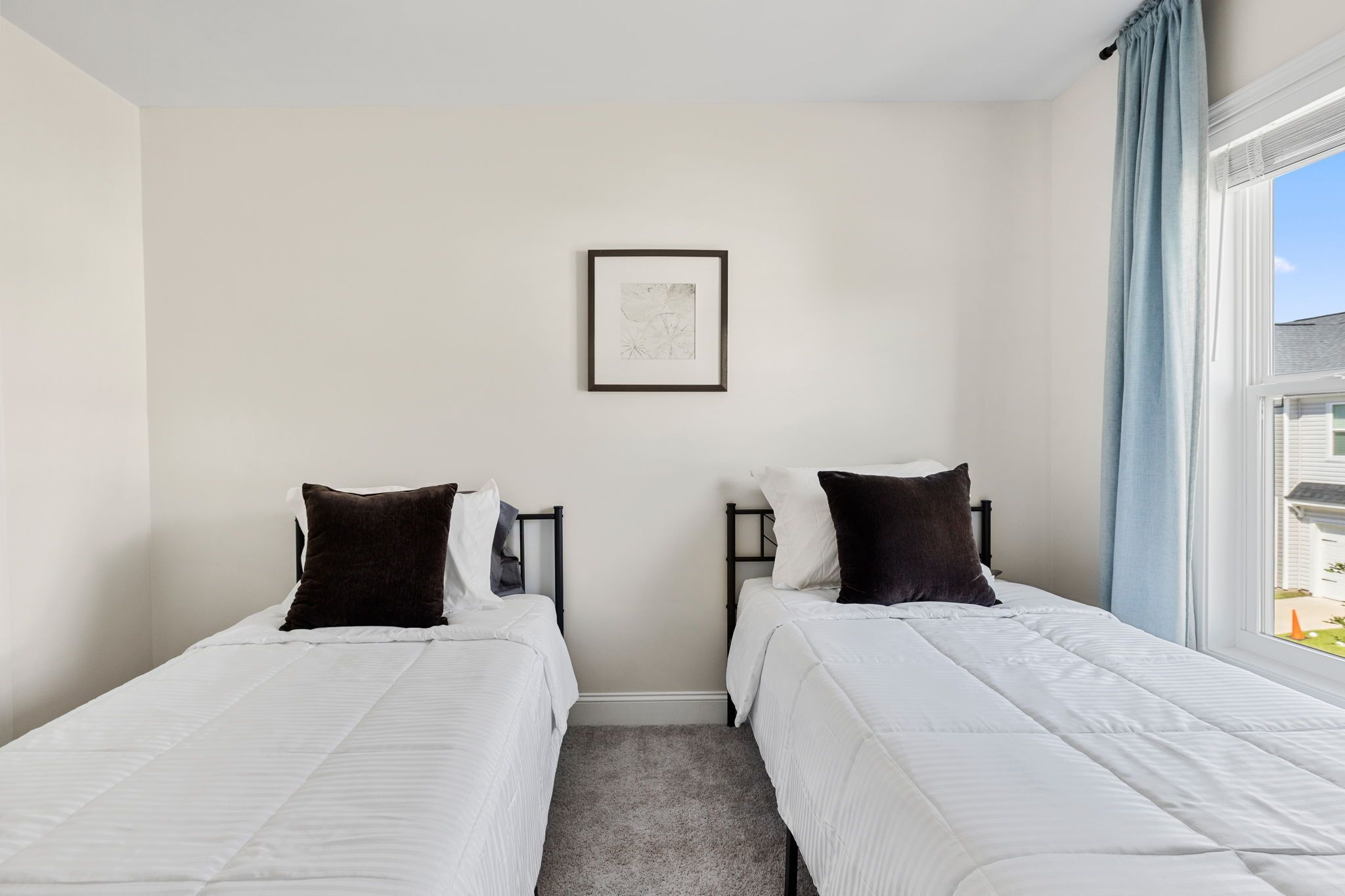 Ein Zweibettzimmer mit zwei Betten, einem gerahmten Bild an der Wand und einem Fenster mit Vorhängen.