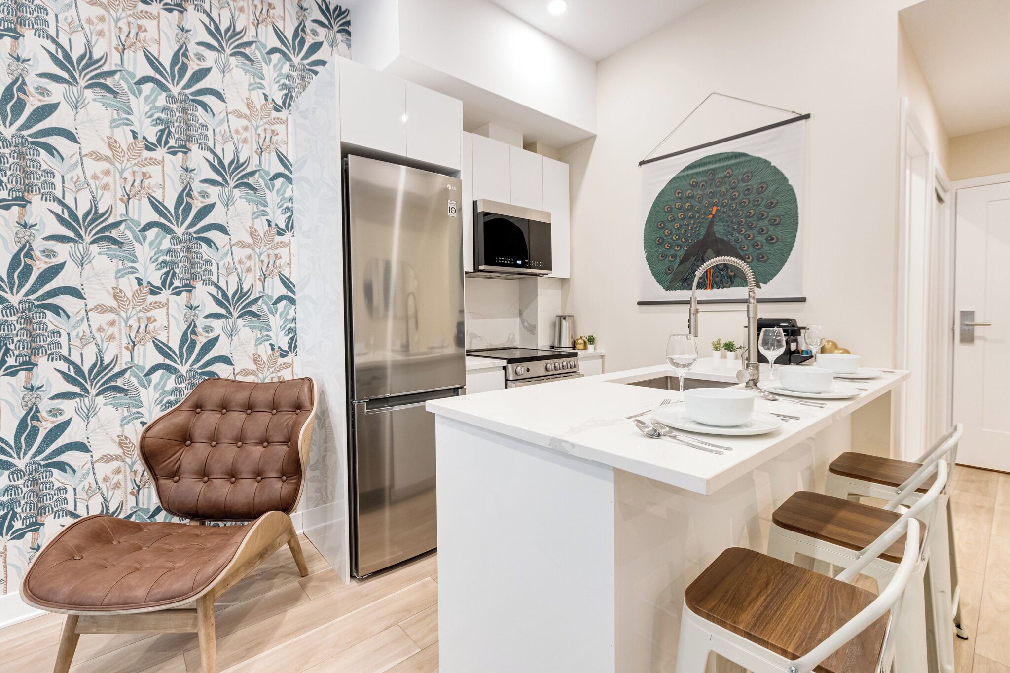 A modern kitchen with a central island, stainless steel appliances, and a decorative peacock wall art.