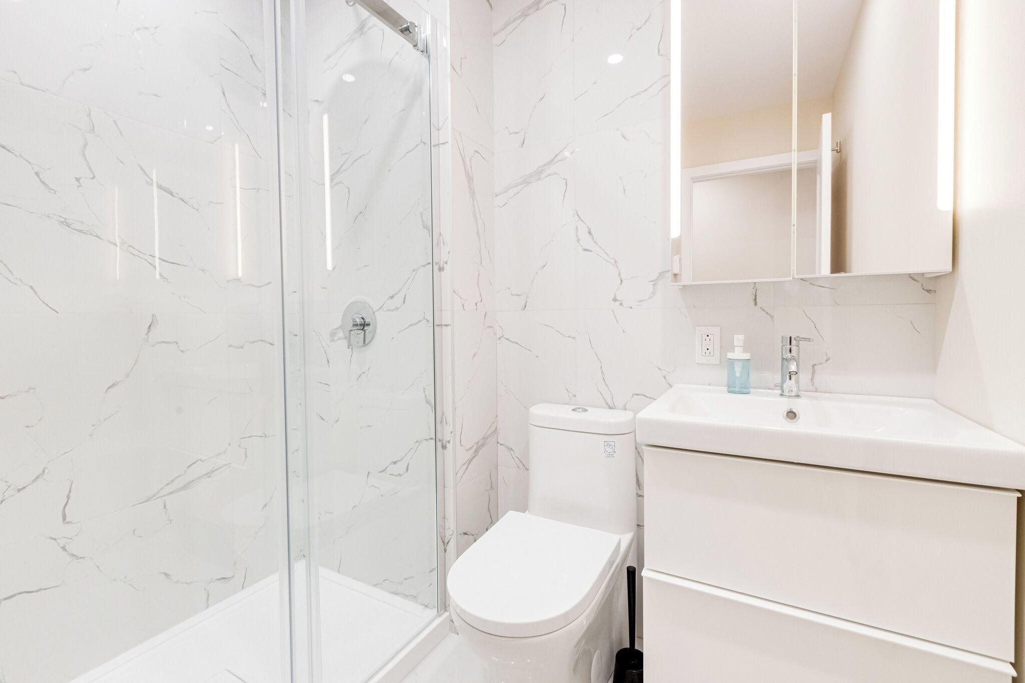 A modern bathroom with a glass shower enclosure, a white toilet, and a vanity with a mirror.