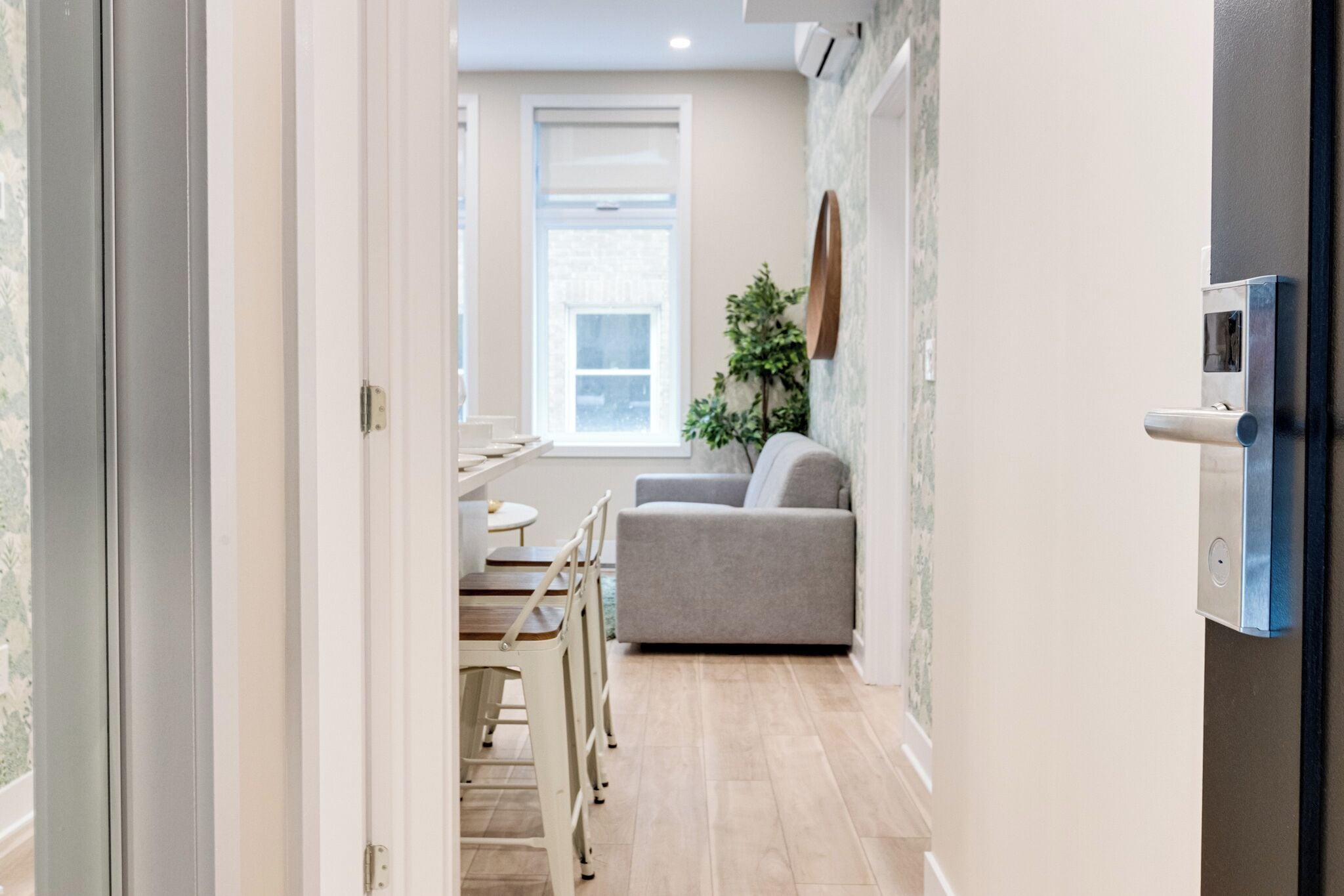 A hallway with a dining area, a sofa, and a wall-mounted TV.