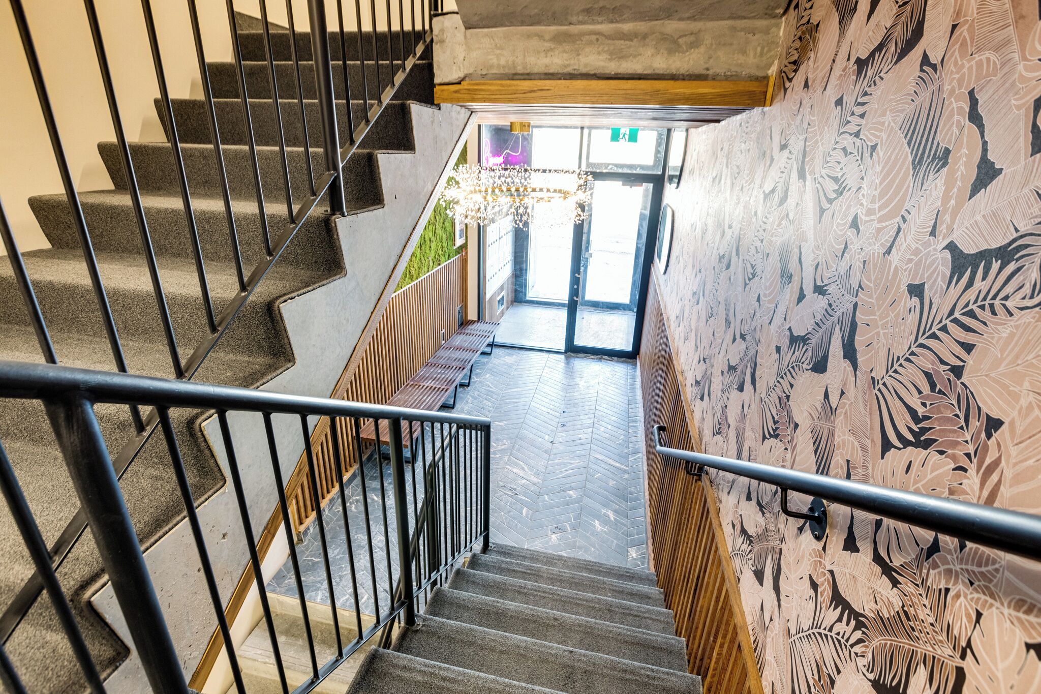 A staircase with a herringbone floor pattern, black metal railings, and a bench at the bottom.