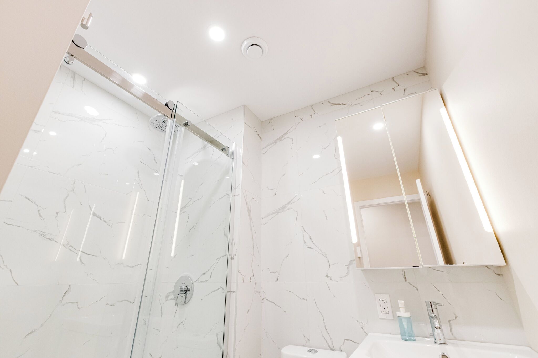 Un bagno moderno con box doccia in vetro, un lavandino bianco con specchio sopra e pareti con decoro in marmo.