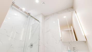 Een moderne badkamer met een douchecabine van glas, een wit wastafelmeubel met spiegel erboven en muren met een marmerlook.
