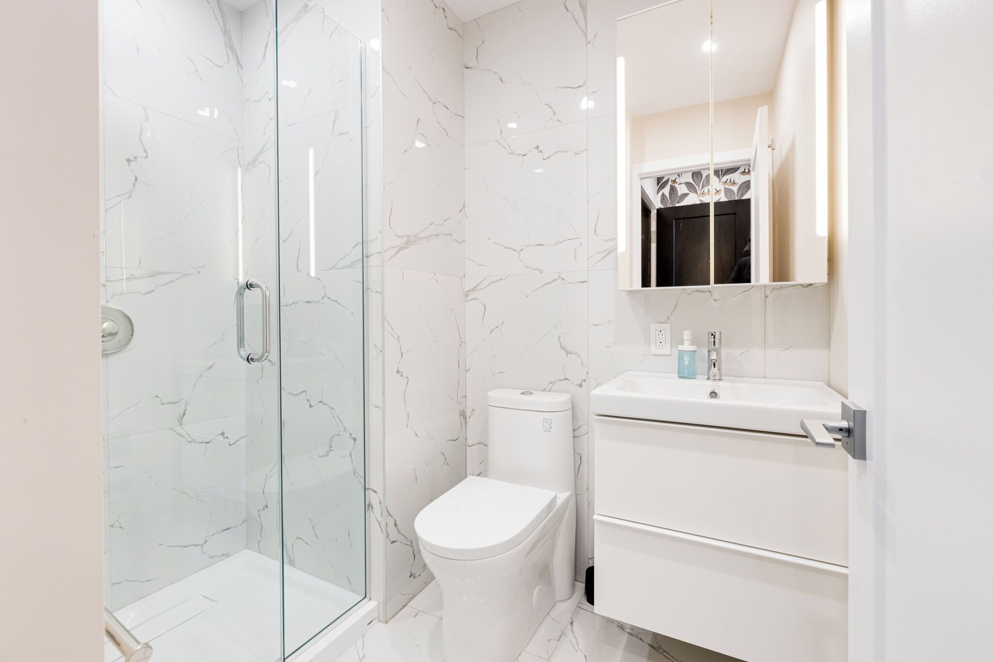 Un baño moderno con cabina de ducha de vidrio, inodoro blanco y tocador con espejo.