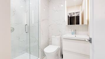 Un baño moderno con cabina de ducha de vidrio, inodoro blanco y tocador con espejo.