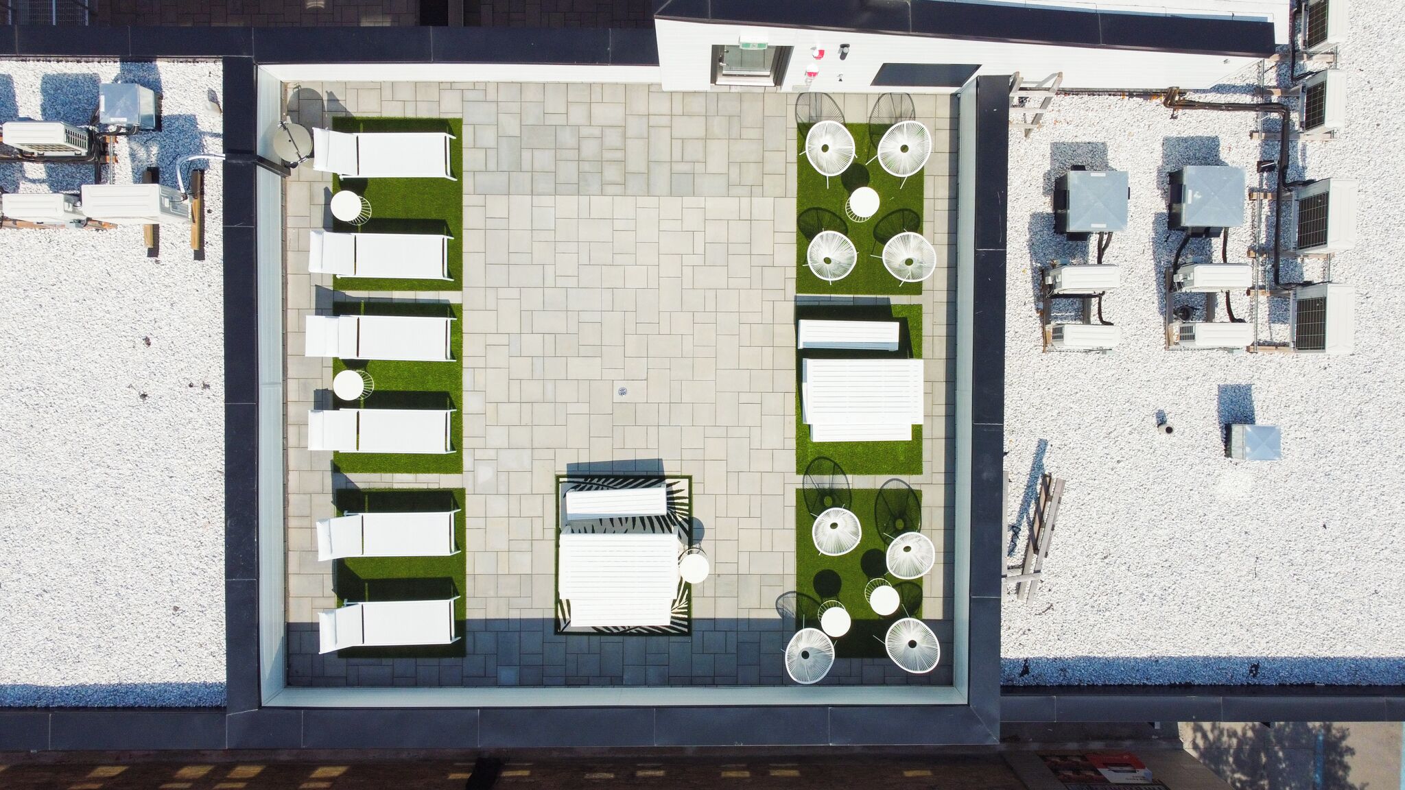 Vue aérienne d’une terrasse sur le toit, avec des espaces aménagés pour s’asseoir, des jardinières et des unités de climatisation.
