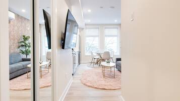 A modern living room with a grey sofa, a TV mounted on the wall, and a dining area with a table and chairs.