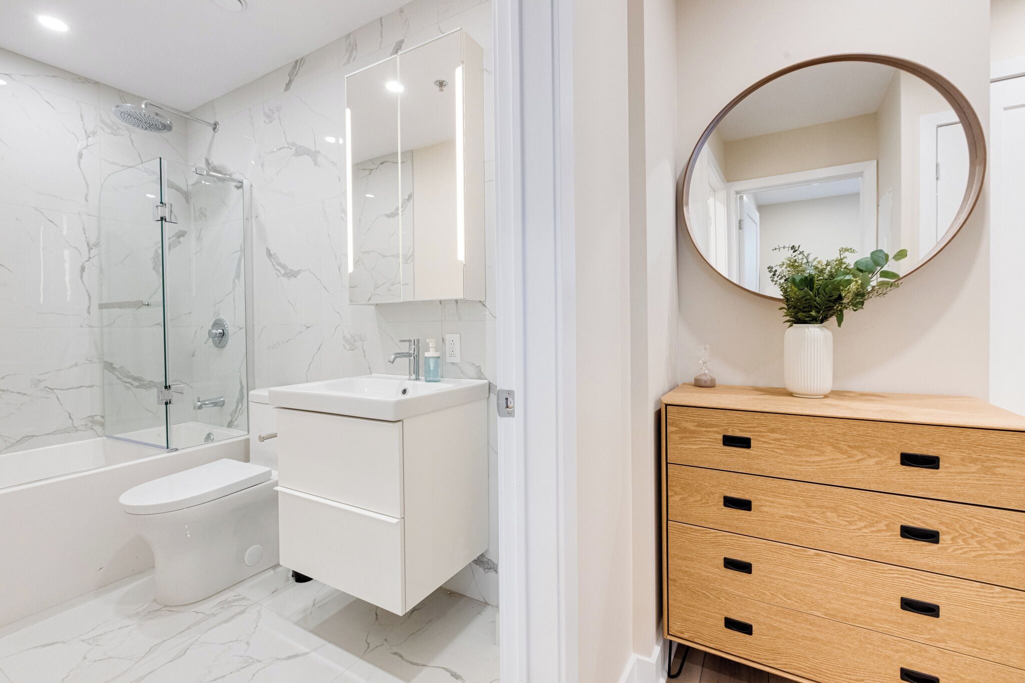 Un bagno moderno con doccia vetrata, un mobile lavabo bianco con specchio e un armadietto in legno.