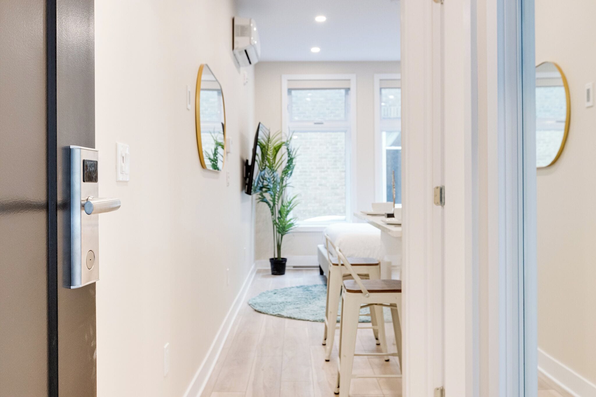 A hallway with a bed, a chair, a plant, and a mirror on the wall.