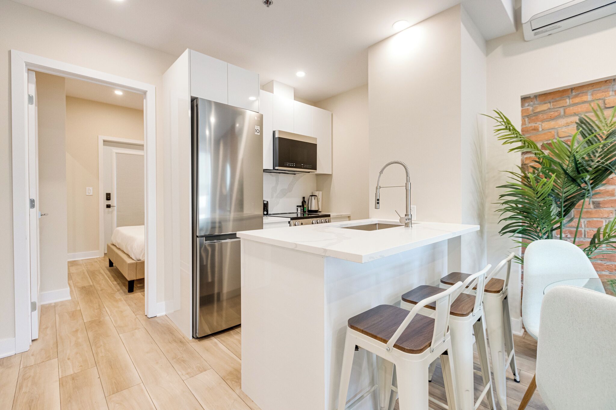 Una cocina moderna con un refrigerador de acero inoxidable, un microondas y un fregadero. Hay una pequeña isla con taburetes de bar y una planta en maceta.