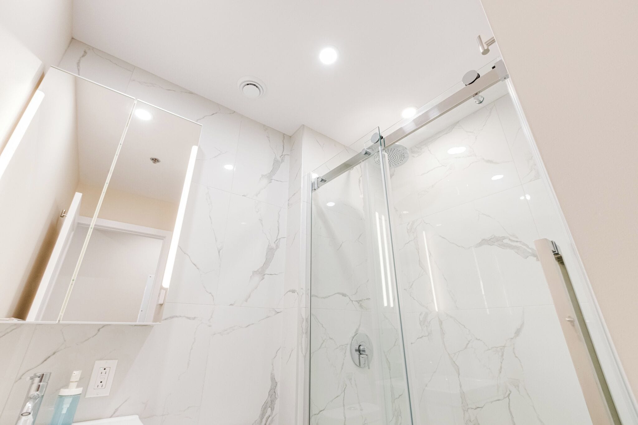 Un bagno moderno con doccia vetrata, pareti in marmo e un'area lavabo in vista con articoli da toilette.