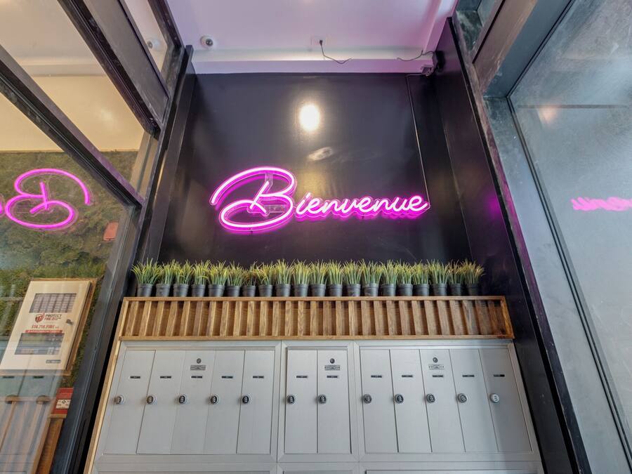 Un área de recepción con un letrero de neón que dice 'Bienvenue', una exhibición de plantas y una fila de casilleros.