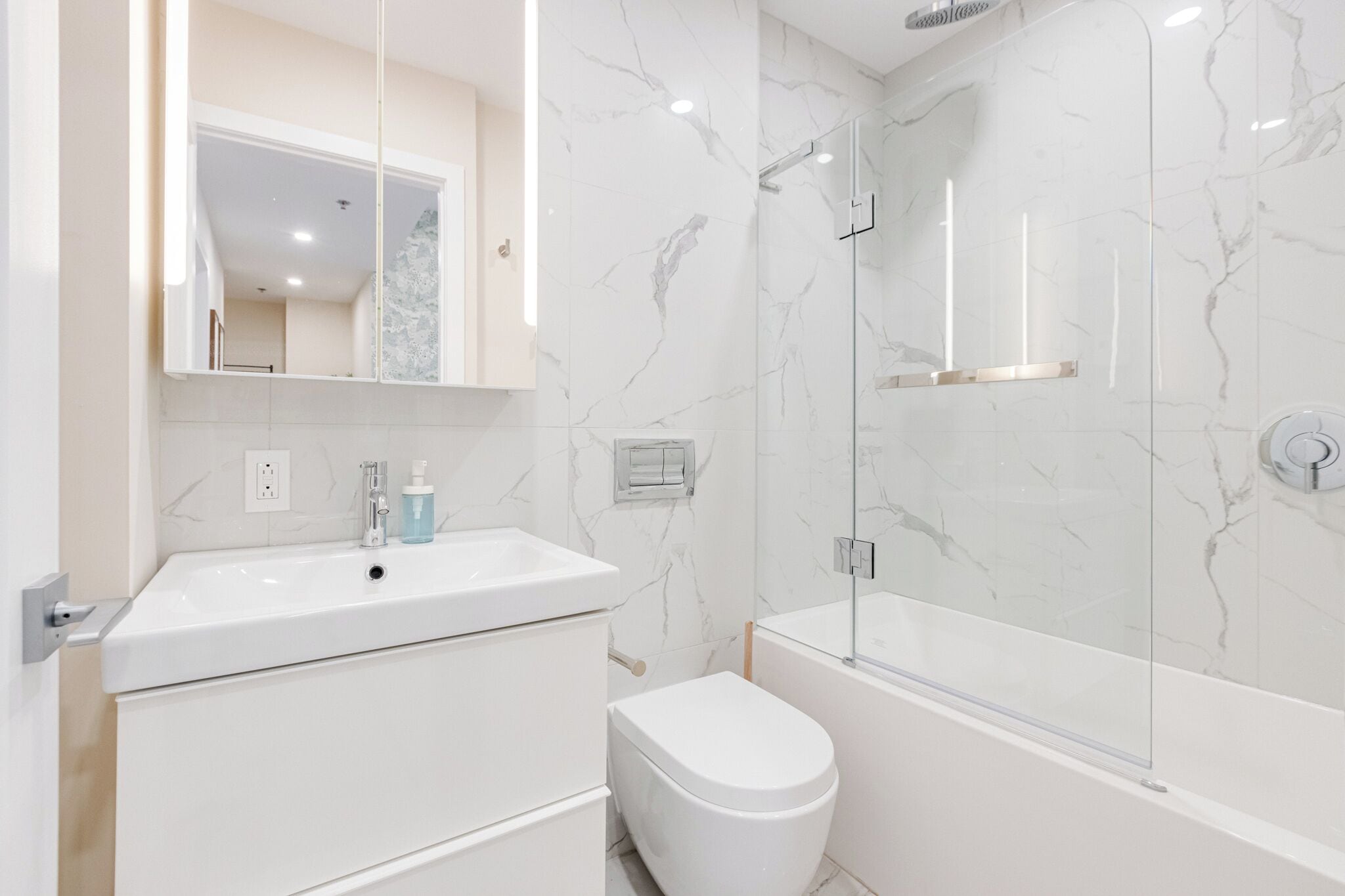 Une salle de bain moderne avec un meuble-lavabo blanc, des toilettes et une douche séparée par une paroi de verre.