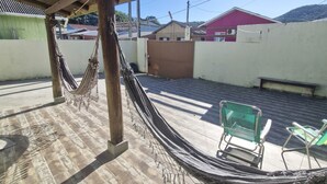 A hammock under a wooden roof, a green chair, and a red building in the background.
