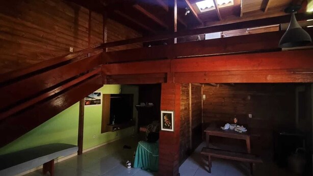 A spacious room with a high ceiling, wooden beams, a green wall, and a tiled floor.