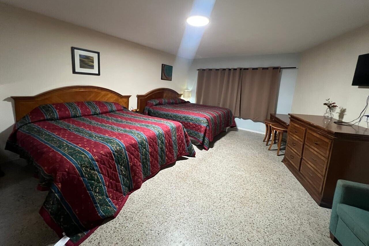 A hotel room with two single beds, a wooden dresser, a desk, and a chair.