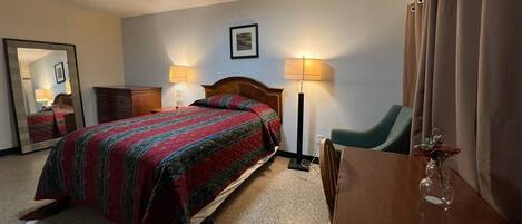 A hotel room with a bed, bedside lamps, a chair, a desk, and a mirror.