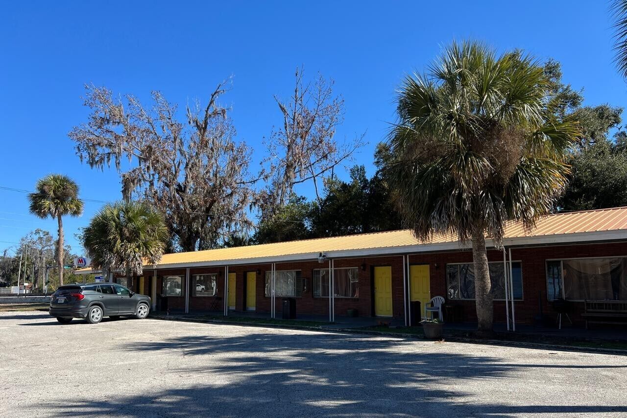 Un motel con fachada amarilla, varias habitaciones y un área de estacionamiento.