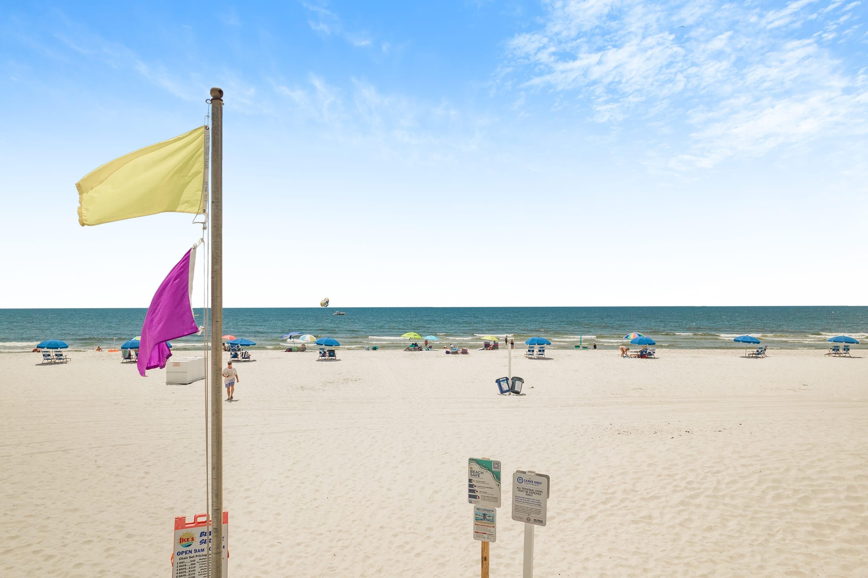 A beach with a flagpole, beach umbrellas, and a clear sky.