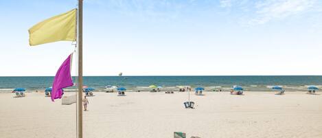 A beach with a flagpole, beach umbrellas, and a clear sky.
