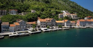 Une ville côtière avec des bâtiments le long du front de mer, un quai où sont amarrés des bateaux et un paysage vallonné en arrière-plan.