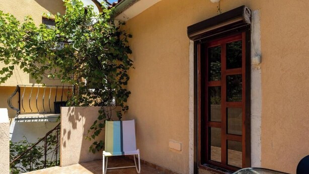 A balcony with a tiled floor, a white chair, a glass table, and a door with a window.