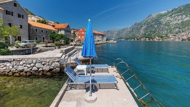 Une zone riveraine avec un quai, des chaises longues et un parasol bleu.