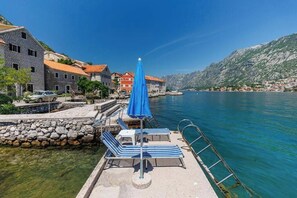 A waterfront area with a dock, lounge chairs, and a blue umbrella.