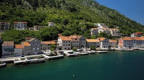 Une ville côtière avec des bâtiments le long du front de mer, un quai où sont amarrés des bateaux et un paysage vallonné en arrière-plan.