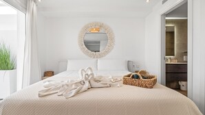 Quarto de hotel com uma cama grande, um espelho redondo, uma cesta de vime e vista para o banheiro.
