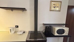 Una cocina compacta con estufa integrada, hervidor, microondas y un cuadro en la pared.