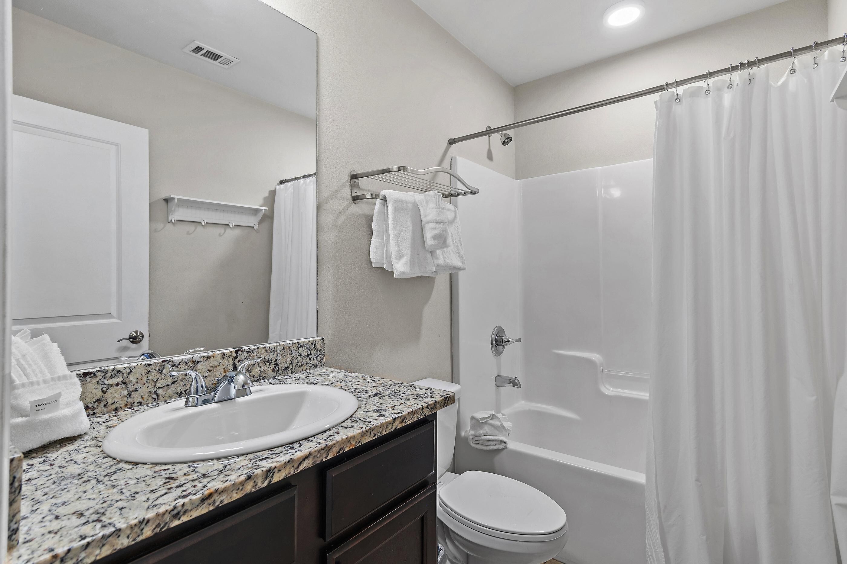 A bathroom with a granite countertop sink, a mirror, a toilet, and a shower curtain.