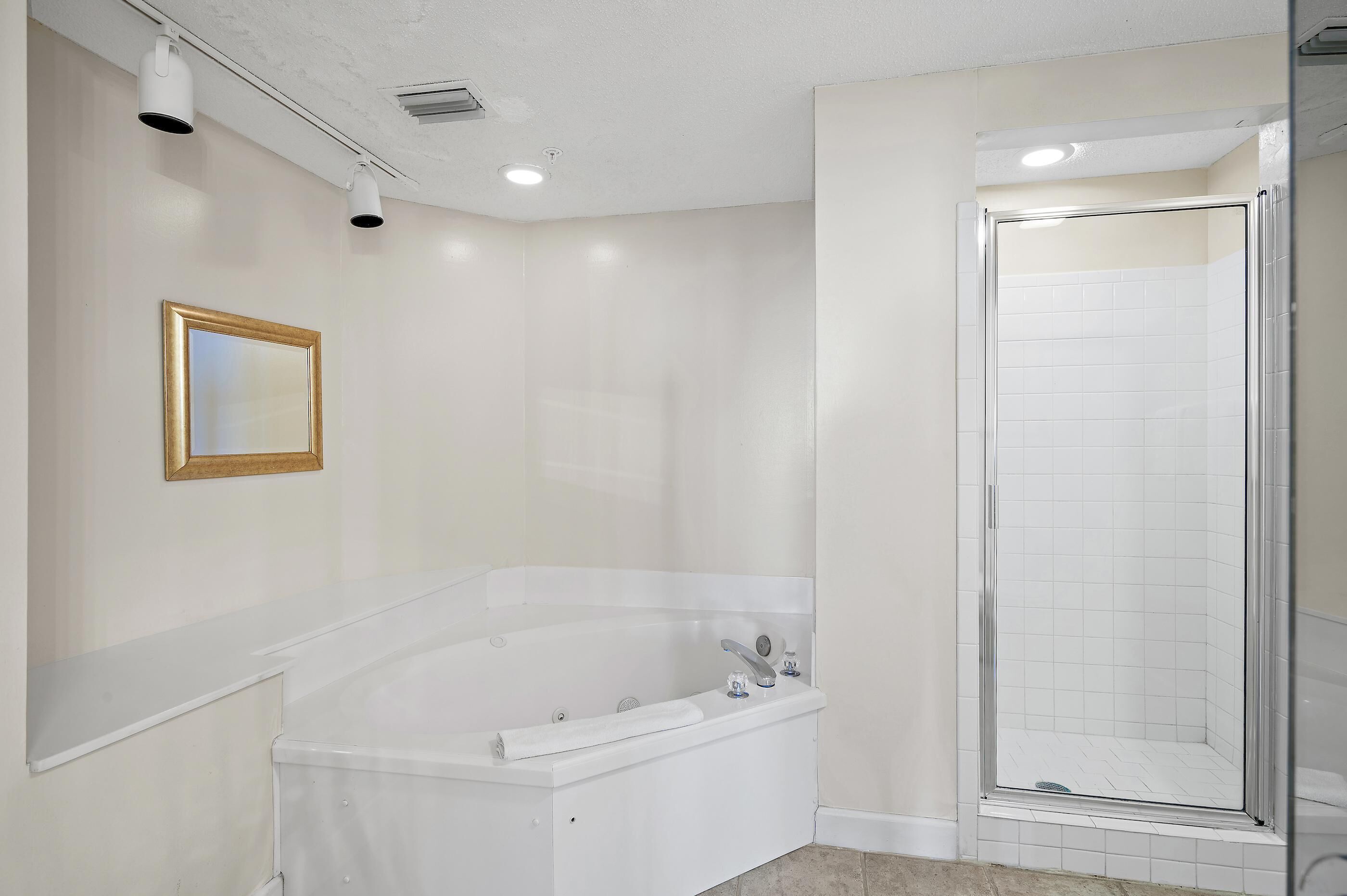 A modern bathroom with a freestanding bathtub, a glass-enclosed shower, and a framed mirror on the wall.
