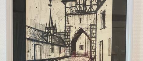 Un dibujo en blanco y negro enmarco muestra una escena callejera con un edificio y una torre.