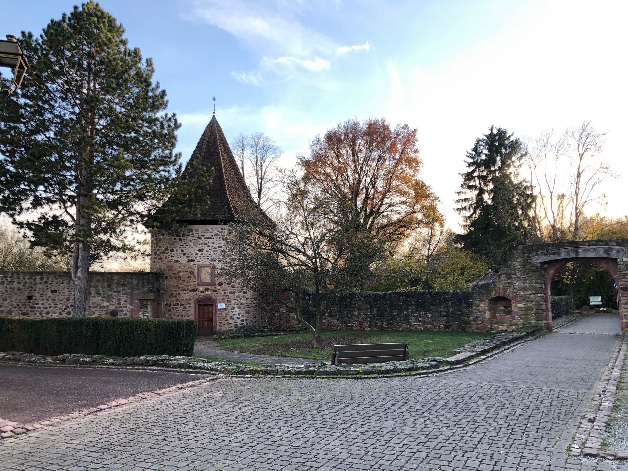 Un bâtiment en pierre surmonté d’un toit conique, avec un banc et un chemin pavé.