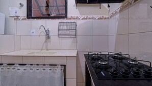 Una cocina con estufa a gas, lavamanos y un ventanal con un vidrio roto.