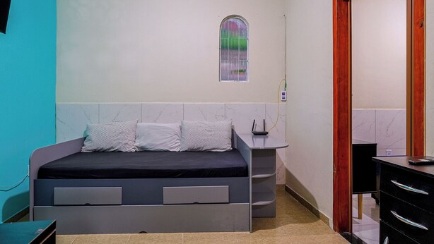 Un dormitorio con una cama, una mesita de noche, una pequeña mesa, una ventana y una puerta.