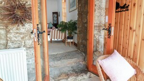 A stone-walled hallway leading to a room with a wooden door, a wicker chair with a cushion, and a potted plant. - Balsaggart Farm (Maybole)