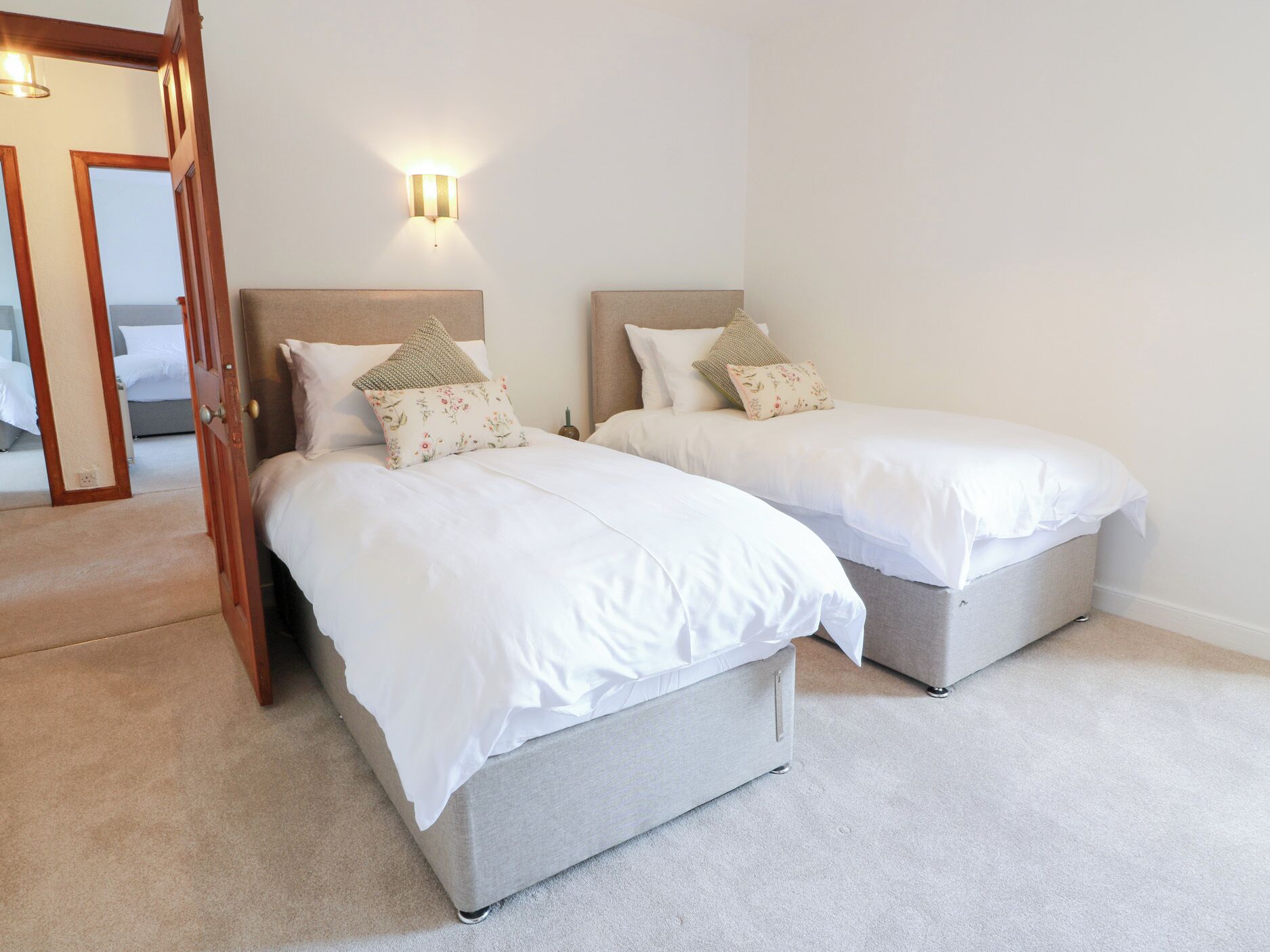 Een slaapkamer met twee eenpersoonsbedden, een houten deur en een wandlamp.
