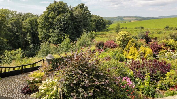 A garden with a variety of plants and flowers, a stone pathway, and a black fence. - Balsaggart Farm (Maybole)