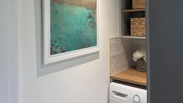 Ein Waschbereich mit Waschmaschine, einem Regal mit Körben und einem gerahmten Gemälde an der Wand.