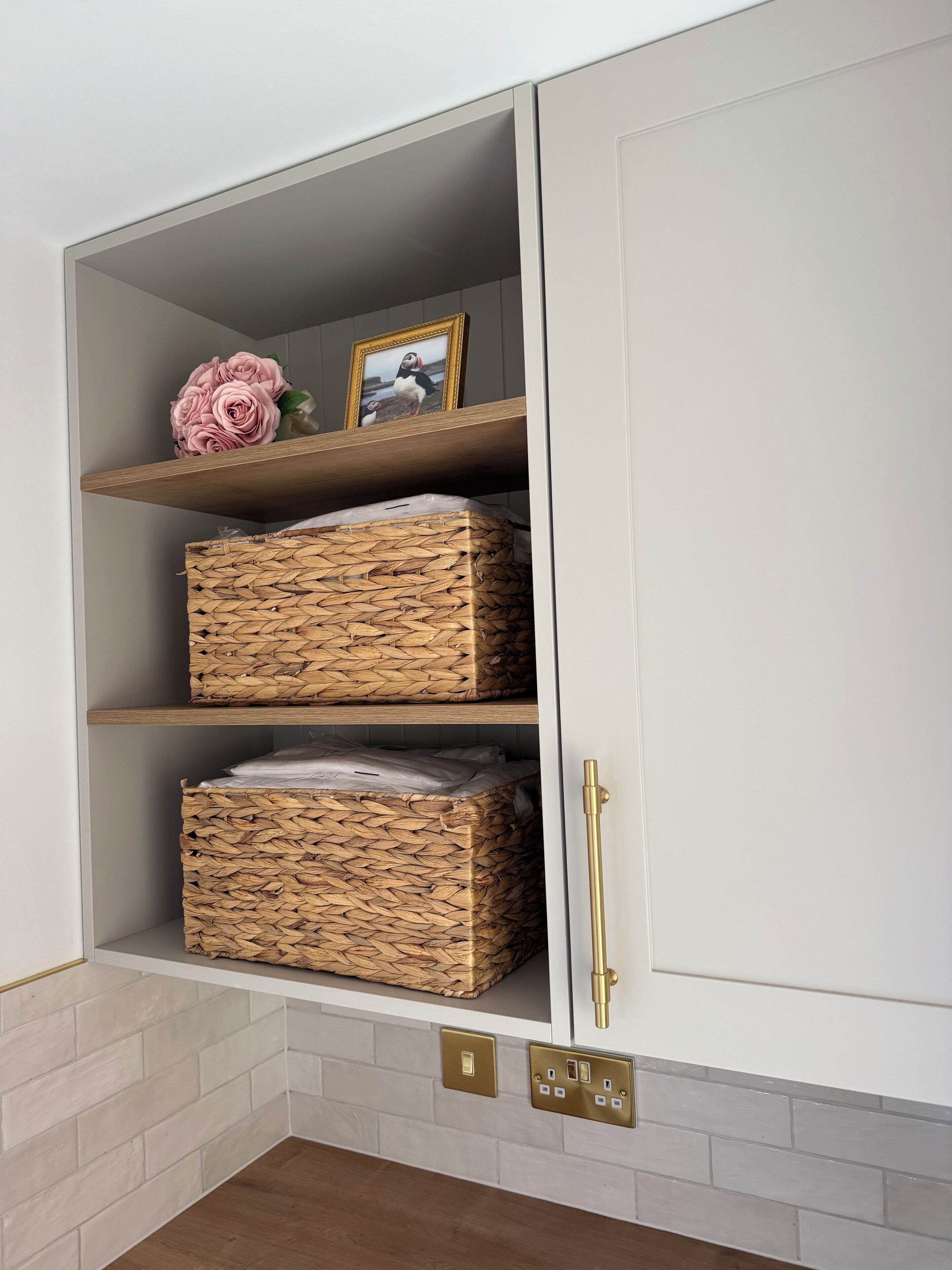 A white cabinet with three wicker baskets on shelves, a picture frame, and a gold handle.