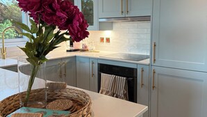 A kitchen with light blue cabinets, a white countertop, and a vase with flowers on a woven tray. - Charming Newly Renovated 1 Bedroom Chalet | Stunning Sea Views (South Whiteness)