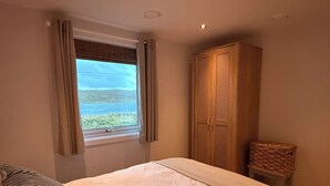 A bedroom with a bed, a window with curtains, a wardrobe, and a wicker chair. - Charming Newly Renovated 1 Bedroom Chalet | Stunning Sea Views (South Whiteness)