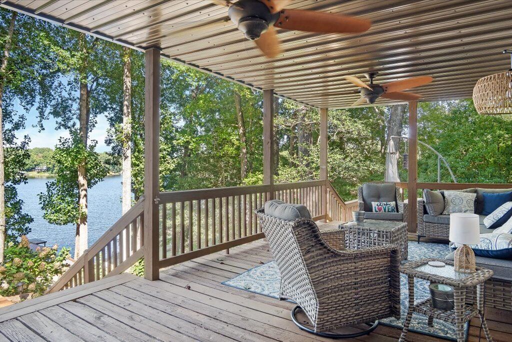 En overdækket terrasse med fletningsmøbler, en ventilator i loftet og udsigt til et sø.