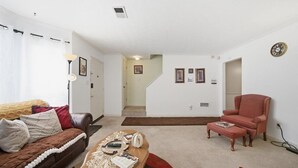 Ein Wohnzimmer mit braunem Sofa, einem roten Sessel, einem Couchtisch und einer Treppe, die in einen anderen Raum führt.