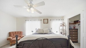 Ein Schlafzimmer mit Bett, Stuhl, Deckenventilator, Kommode und Fenster.