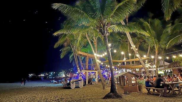 Un restaurante frente a la playa con terraza y palmeras.