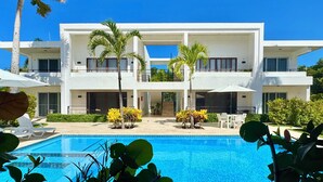 Un hotel moderno de dos pisos con piscina, palmeras y mobiliario exterior.