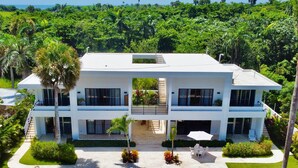 Una casa moderna de dos pisos con piscina, rodeada de exuberante vegetación y palmeras.